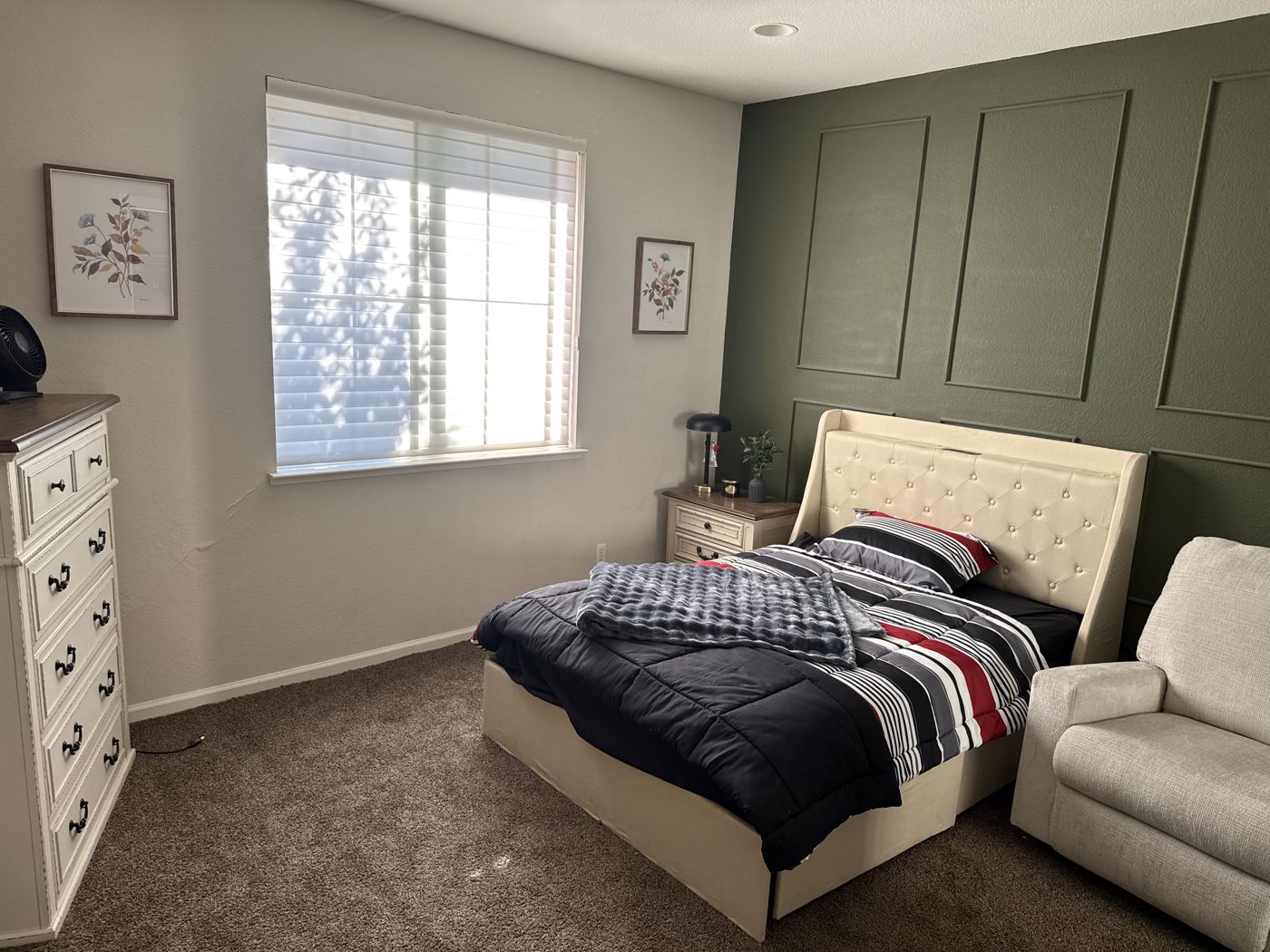Private bedroom with a tufted bed, dresser, large window, and a green accent wall.