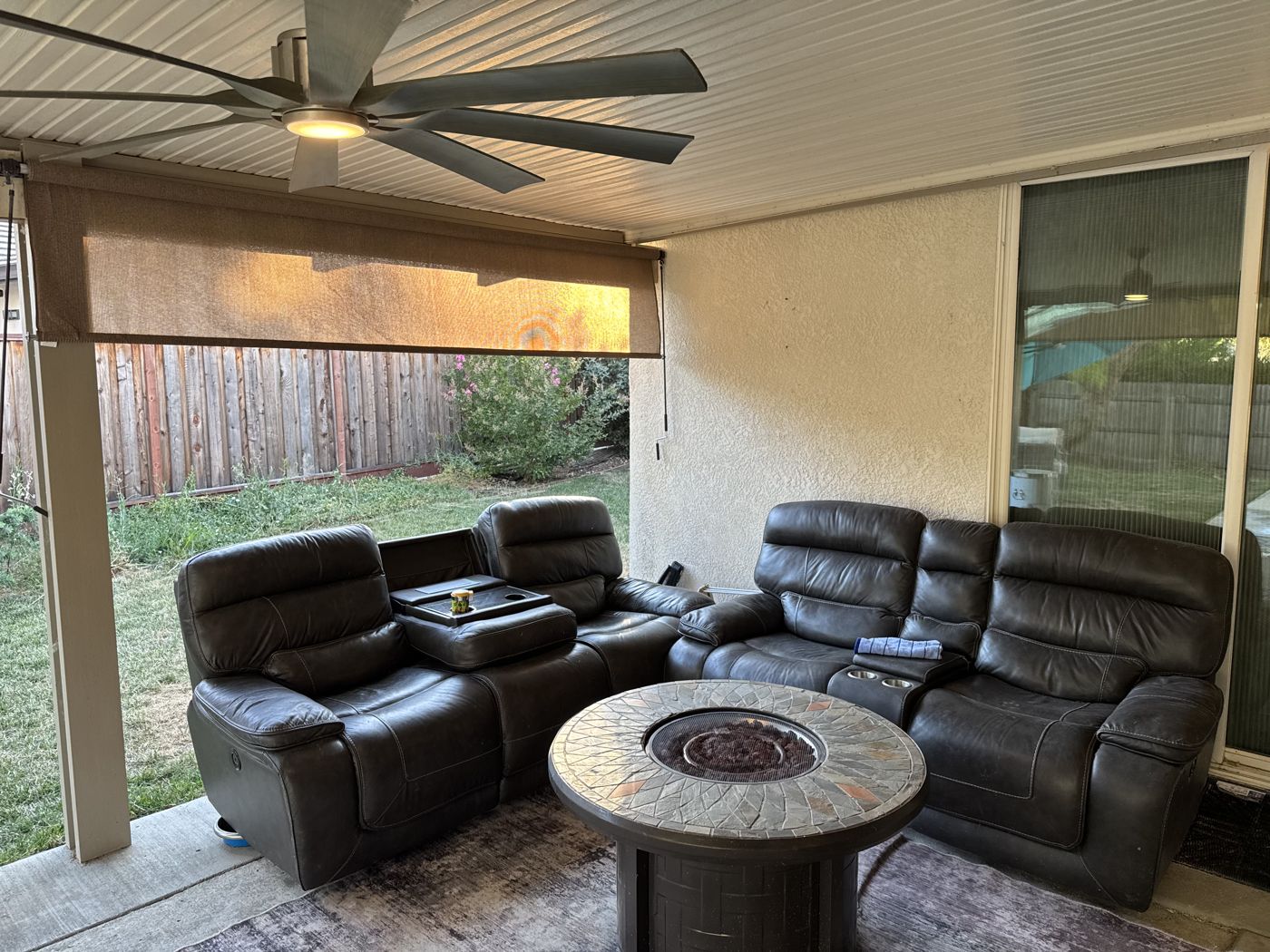 Covered back patio with leather seating and a stone fire-pit table overlooking the yard.